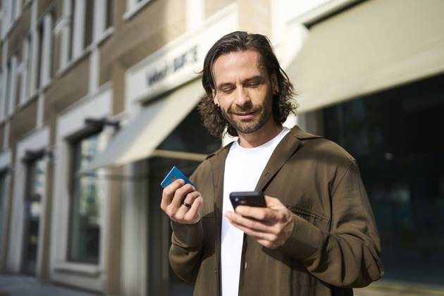 Smiling mature man using smart phone doing online shopping through credit card on sunny day model released, Symbolfoto, PNEF02939