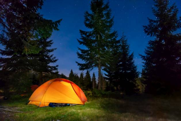 Orange illuminated tent in dark night forest with night sky and stars ,model released, Symbolfoto