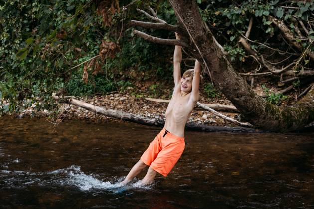 IMAGO Creative, Jahreszeit Sommer, Sommerferien Smiling child swinging on tree branch over river during summer Glenallen, Missouri, United States CR_WEKW240709-1474545-01 ,model released, Symbolfoto