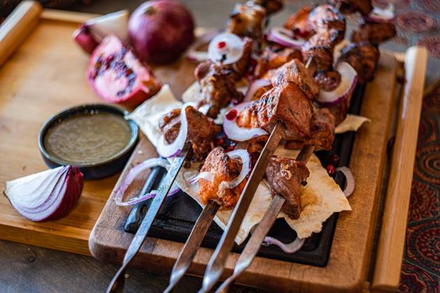 A rustic presentation of Georgian mtsvadi, showcasing succulent grilled meat skewers, served on a wooden board with sliced onions, pomegranate seeds, and traditional flat bread Perfect for culinary themes Model Released AnnaBogush_ID22661_660722_004 Copyright: xAnnaxBogushx