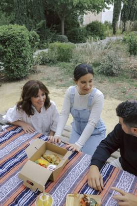 MR_ID21763_17423_LaraMartinez.jpg, MR_ID21763_17422_CarmenGomez.jpg, MR_ID21763_17425_MiguelSarrio.jpg, MR_ID21763_17424_ClaudiaAlcantarilla.jpg Friends enjoy a relaxing picnic outdoors among lush greenery. One woman, dressed in white with brown hair, and a second in blue overalls, are both looking at an open box of assorted pastries on a picnic blanket Model Released LuisTenza_ID21763_638535_017 Copyright: xLuisxTenzax RECORD DATE NOT STATED