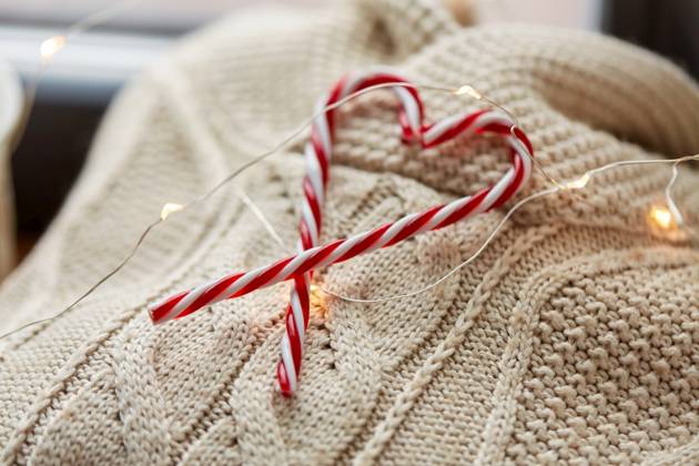 christmas, clothes and objects concept - close up of warm wool braided sweater, candy cane and electric garland string at home. close up of sweater, candy cane, christmas garland ,model released, Symbolfoto