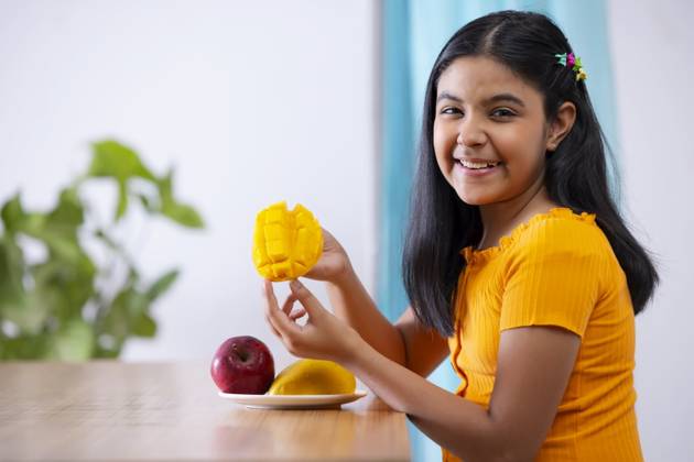 Portrait of cheerful girl holding a segmented slice of mango ,model released, Symbolfoto
