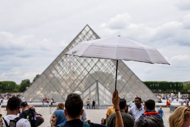 IMAGO Creative, Jahreszeit Sommer, Hitze Paris, France - July 14, 2024: In front of the Louvre Museum in Paris, tourists protect themselves from the summer heat with a parasol while queuing in front of the famous glass pyramid