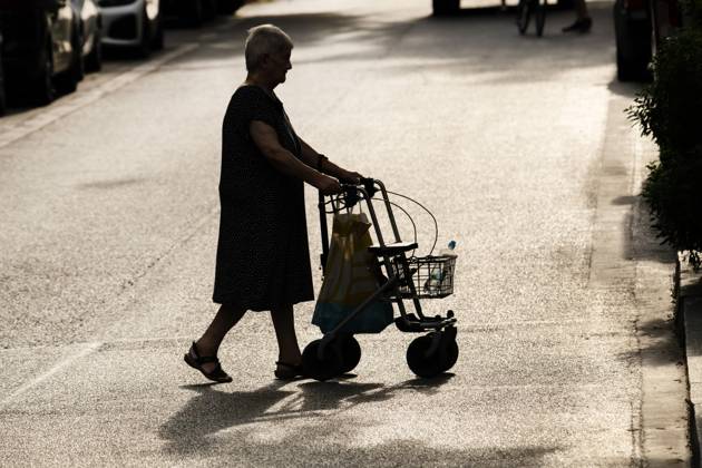 old woman with rollator walking in the city in the summer heat, July 2024 Germany, Munich, July 2024, old woman with rollator walking in the heat, in the summer heat there is a risk of dehydration, especially for older people, senior citizen has taken a water bottle with her, strong sunlight, back