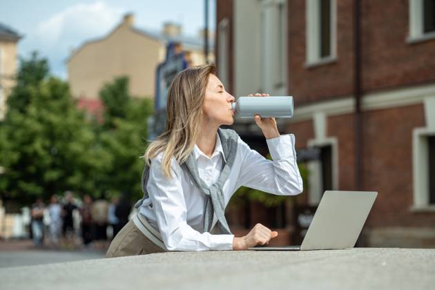 IMAGO Creative, Jahreszeit Sommer, Hitze Happy woman with laptop outside drinking water from bottle, coping with dehydration, thirst. Businesslike girl using computer, working outside, enjoying fresh air, warm weather. Satisfied smiling woman replenishes balance of fluids in body by drinking water with pleasure at hot summer day. ,model released, Symbolfoto Copyright: xZoonar.com DmitriixMarchenkox 22036083 ,model released, Symbolfoto ,property released
