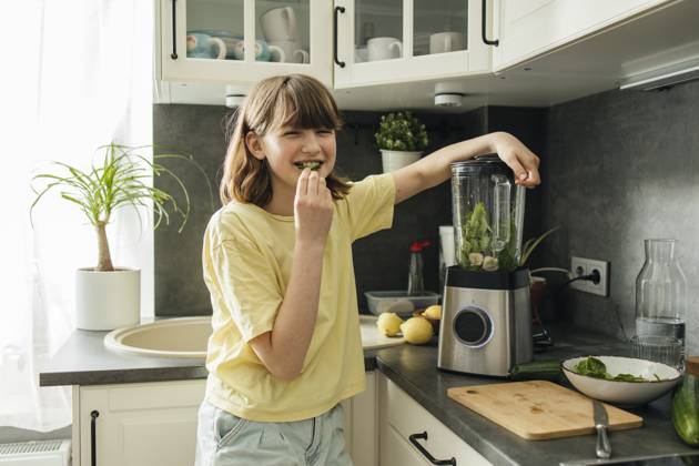 Smiling girl eating spinach leaf and making smoothie in kitchen at home model released, Symbolfoto property released, ELMF00669