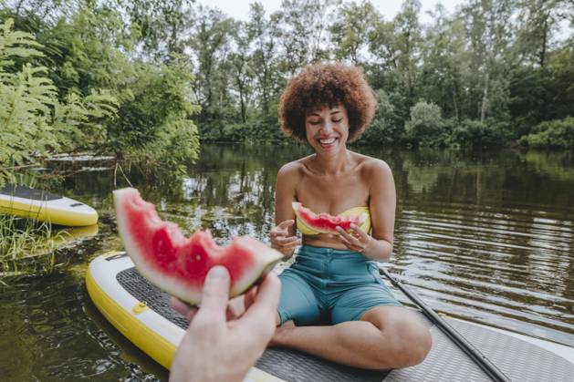 Happy woman eating watermelon with friend on paddleboard in lake model released, Symbolfoto, YTF01036