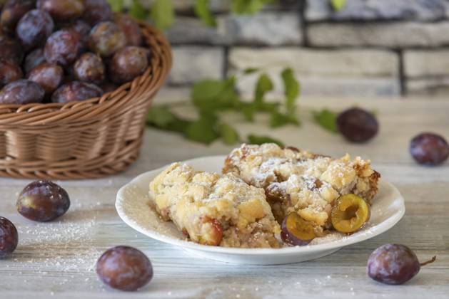 IMAGO Creative, Herbst, Food, Pflaumenkuchen Zwetschgenkuchen auf einem Teller neben Korb mit frischen Zwetschgen im Hintergrund, auf einem weißen rustikalen Tisch Plum cake on a plate next to a basket with fresh plums in the background, on a white rustic table Copyright: imageBROKER LucasxSeebacher ibxlse11118372.jpg