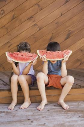 Boy and girl hiding faces with watermelon slices and sitting at porch model released, Symbolfoto, ONAF01016