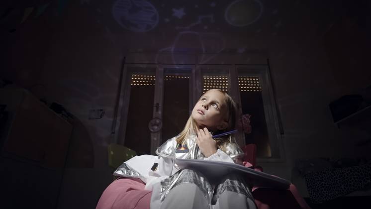 Thoughtful astronaut girl with paper fantasizing in dark bedroom at home model released, Symbolfoto property released, ZEDF04956