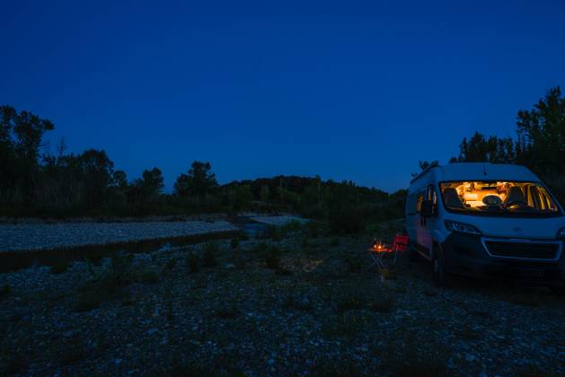 A man sits on a camping chair in front of a table on a blue hour summer evening in front of his campervan Germany On the road in a campervan