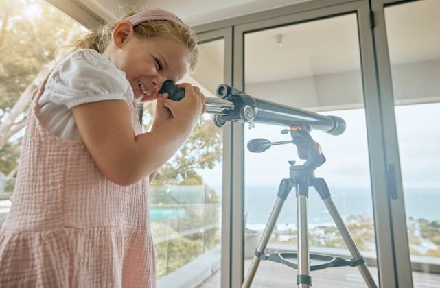 Young kids, telescope and home learning about planets, stars and sky in space. Excited, curious and happy girl play, watch and study view of universe, science and moon for fun educational development. model released property released Copyright: xwww.peopleimages.comx