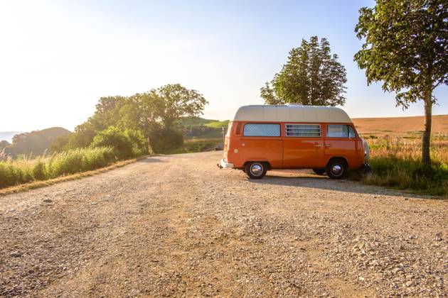 An orange and white VW Bus van stands on a gravel parking lot on a summer morning, Baden Württemberg, Germany A van stands in the landscape