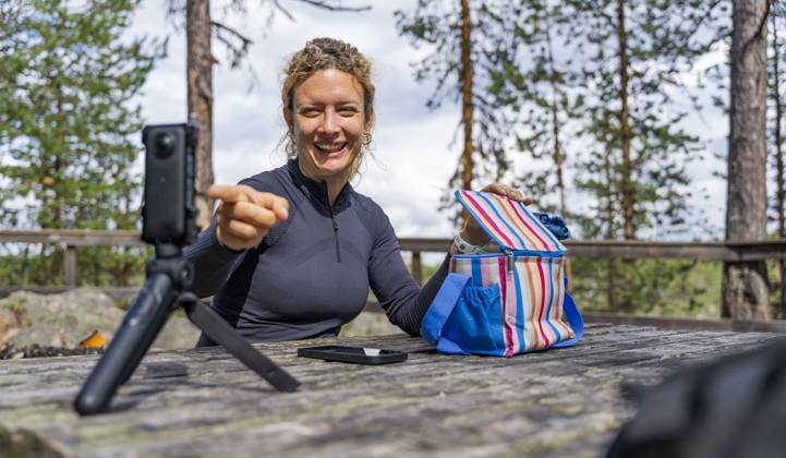 A joyful woman relishes her lunch outdoors while trekking in the serene Muddus National Park, located in Lapland, Sweden She is capturing the moment using a camera on a tripod Model Released VictorCuenca_ID24674_714855_004 Copyright: xVictorxCuencax