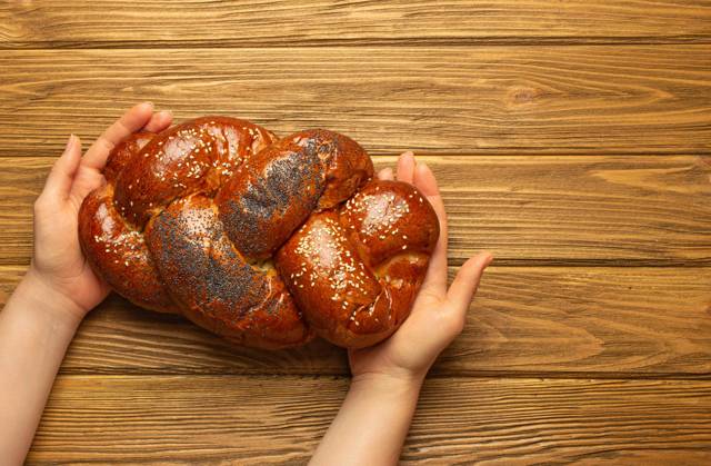 Weibliche Hände halten frisch gebackenes Challah-Brot mit Mohn- und Sesamkörnern, Draufsicht auf rustikalen Holzhintergrund, traditionelle festliche jüdische Küch Female hands holding freshly baked Challah bread covered with poppy and sesame seeds, top view on rustic wooden background, traditional festive Jewish cuisine. Copyright: xZoonar.com OlenaxYeromenkox 22313048