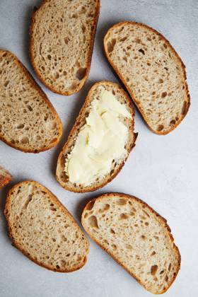 Top view of sliced fresh homemade sourdough bread with some slices generously spread with butter, set on a grey textured surface. Model Released TwoInspirations_ID26492_764459_013 Copyright: xTwoxInspirationsx RECORD DATE NOT STATED