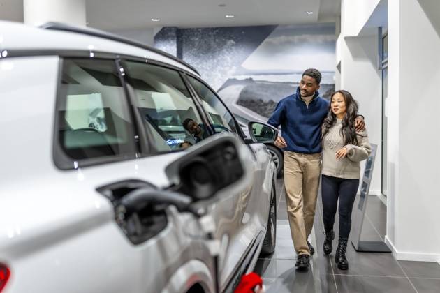 Ein multiethnisches Paar geht durch ein Autohaus und wählt fröhlich sein neues Elektrofahrzeug aus, während es den modernen Ausstellungsraum genießt Multiethnic couple walking through a car dealership, happily selecting their new electric vehicle while enjoying the modern showroom experience Copyright: imageBROKER UnaixHuizi ibxuhu12460353.jpg ,model released, Symbolfoto ,property released