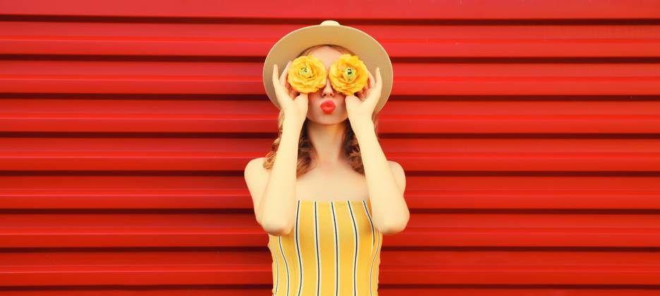 Sommer Porträt der stilvollen jungen Frau bläst Kuss mit gelben Blütenknospen auf rotem Hintergrund Summer portrait of stylish young woman blowing kiss with yellow flower buds looking for something in round straw hat on red background ,model released, Symbolfoto Copyright: xZoonar.com VeronikaxKornevax 22936412 ,model released, Symbolfoto ,property released
