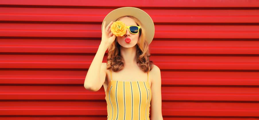 Sommer Porträt der stilvollen jungen Frau bläst Kuss mit gelben Blütenknospen auf rotem Hintergrund Summer portrait of stylish young woman blowing kiss with yellow flower buds looking for something in round straw hat on red background ,model released, Symbolfoto Copyright: xZoonar.com VeronikaxKornevax 22936424 ,model released, Symbolfoto ,property released