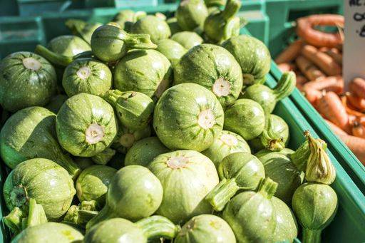 Fresh round zucchinis displayed in a green crate at a vibrant farmers market, capturing the essence of local produce. 28945542 RECORD DATE NOT STATED