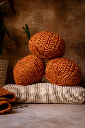 Three warm-toned yarn balls sit elegantly on a knitted surface, evoking cozy autumn vibes. The background features natural elements, enhancing the rustic charm. Model Released CintiaViudez_ID26646_768872_005 Copyright: xCintiaxViudezx RECORD DATE NOT STATED