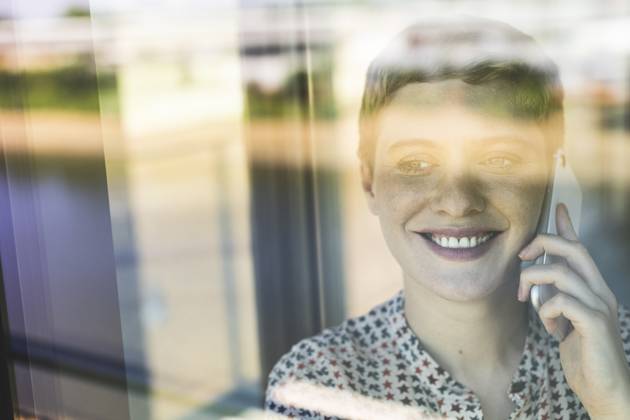 Close-up of smiling businesswoman talking over smart phone in office seen through window model released, Symbolfoto property released, UUF21521