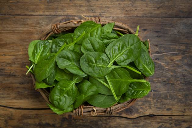 Fresh baby spinach in a willow basket on a wooden background, LVF09447
