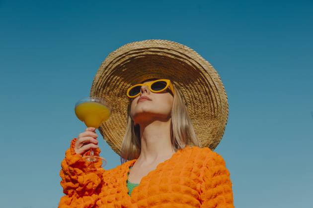 Stylish woman in orange clothing and straw hat enjoying a cocktail outdoors model released, Symbolfoto, VSNF03025