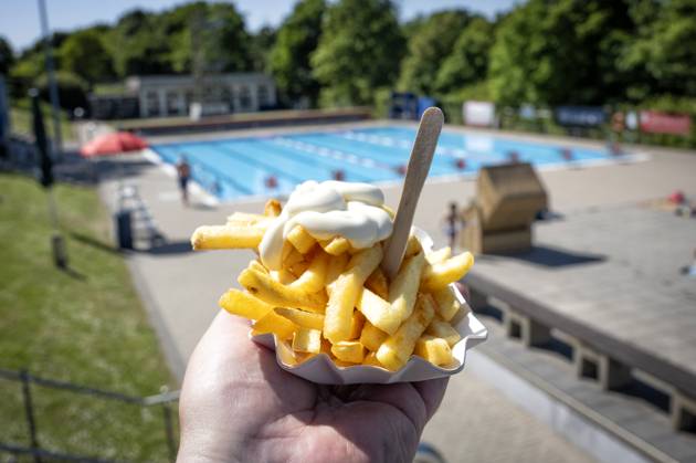 Outdoor pool fries Fresh fries with mayonnaise in a typical white cardboard bowl are held by a hand in t