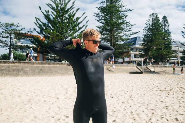 Man in wetsuit smiling on sunny beach near modern buildings Manly, New South Wales, Australia CR_MGTP250515B-1727293-01 ,model released, Symbolfoto