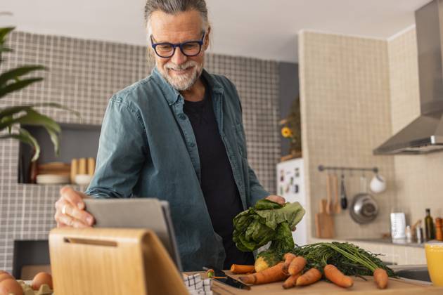 Mature man using a tablet while preparing vegetables in a modern kitchen model released, Symbolfoto property released, JCCMF13550