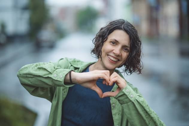 Smiling woman making heart symbol in city on rainy day model released, Symbolfoto, ANAF04798