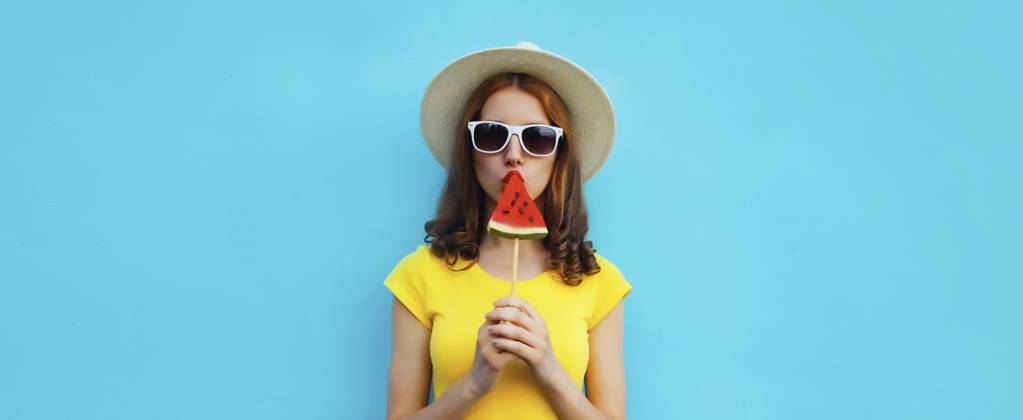 Sommer Porträt der stilvollen jungen Frau mit süßen saftigen Lutscher oder Eis geformt Scheibe Wassermelone trägt Strohhut auf blauen Studio Hintergrund Summer portrait of stylish young woman with sweet juicy lollipop or ice cream shaped slice of watermelon wearing straw hat on blue studio background Copyright: imageBROKER VeronikaxKorneva ibxiqx14269580.jpg ,model released, Symbolfoto ,property released