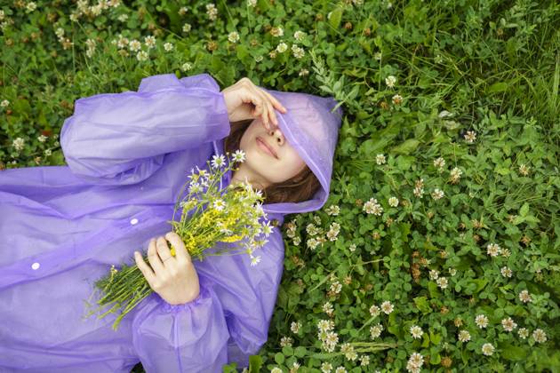 Creative Highlight Symbolbilder Woman in purple raincoat relaxing on grass with wild flowers in summer model released, Symbolfoto, VCF00802