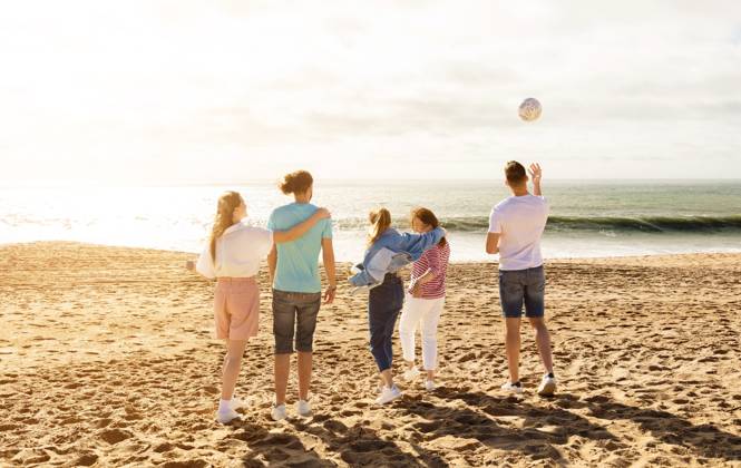 Friends enjoying a sunny day at the beach while playing with a ball A group of five friends stands on the sandy beach, enjoying a sunny day. They are playing with a ball and laughing as the waves crash gently behind them., model released, , 63323714.jpg RECORD DATE NOT STATED