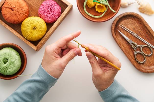 Top view of a woman crocheting in her artisan studio Top view of cropped unrecognizable hands of a woman crocheting in her studio. Surrounded by colorful yarn and crochet tools, she crafts intricate handmade designs. Model Released Natanordic_ID30668_1037815_002 Copyright: xNatanordicx RECORD DATE NOT STATED