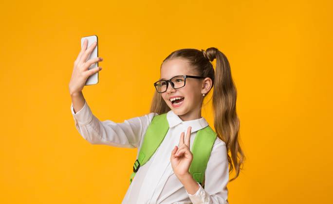 Schoolgirl Using Smartphone Taking Selfie Gesturing V-Sign, Yellow Background School Selfie. Happy Schoolgirl Using Smartphone Taking Self-Portrait Gesturing Victory Sign On Yellow Studio Background. Copy Space, model released, , 60918330.jpg RECORD DATE NOT STATED