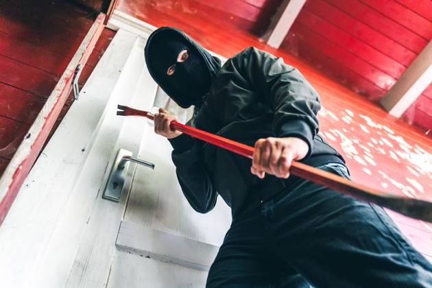 Bavaria, Germany - August 26, 2025: Masked burglar stands in front of a front door with a crowbar. Symbolic image for burglary and robbery