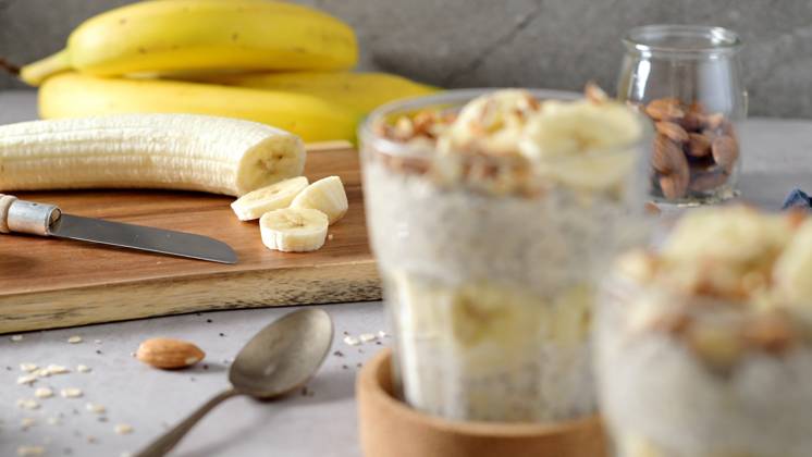 IMAGO Creative, Food, High Protein Frühstück Two bowls of overnight oats topped with banana slices and almonds Two bowls of overnight oats topped with banana slices and almonds. A spoon, cutting board, knife, and a blue napkin rest nearby., 63441024.jpg RECORD DATE NOT STATED