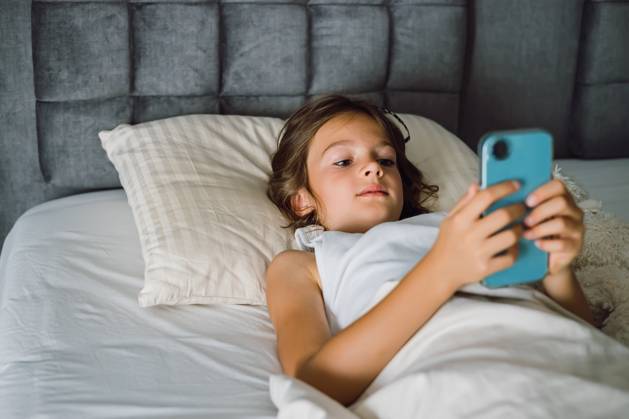 Ein junges Mädchen konzentriert sich auf ihr Smartphone, während es sich im Bett entspannt. Konzept: Bildschirmzeit, digitale Gewohnheiten und modernes Leben zu Hause A young girl focused on her smartphone while relaxing in bed. This photo captures a common scene of childhood and technology, suitable for topics of screen time, digital habits, and modern home life (License=RF) ,model released, Symbolfoto Copyright: xZoonar.com AnnaxLuryex 24043367 ,model released, Symbolfoto ,property released