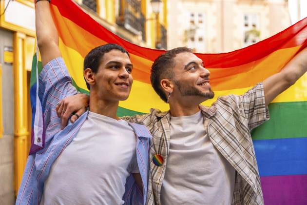 Zwei lächelnde Männer, die sich umarmen und stolz die leuchtende Regenbogenflagge zeigen, die bei einer öffentlichen Demonstration für die Rechte von Lesben und Schwulen, für Liebe und Vielfalt steht Two smiling men embracing and proudly displaying the vibrant rainbow flag, symbolizing lgbtq plus rights, love, and diversity during a public demonstration Copyright: imageBROKER UnaixHuizi ibxuhu15317626.jpg ,model released, Symbolfoto ,property released