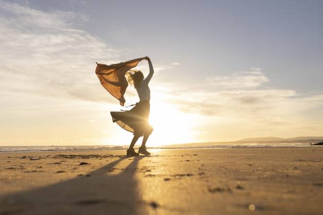 A woman stands on a beach with a scarf around her neck A woman stands on a beach with a scarf around her neck. The sky is a beautiful orange color, and the sun is setting. The woman is enjoying the moment and the beautiful scenery, 60897446.jpg RECORD DATE NOT STATED