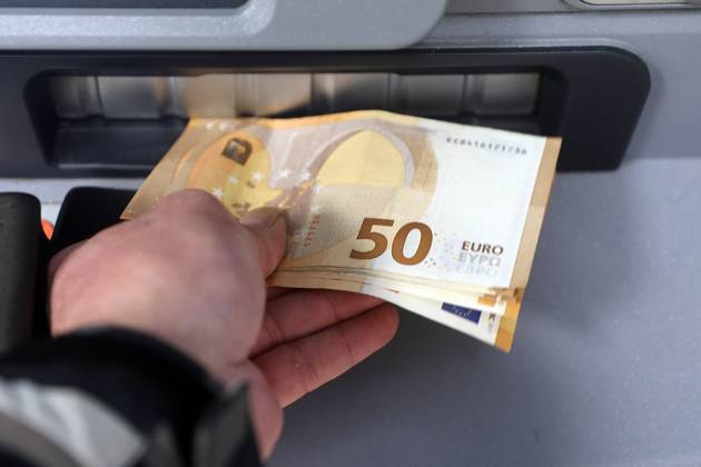 Cash supply from an ATM A person withdraws a large amount of cash in 50 euro bills from an ATM