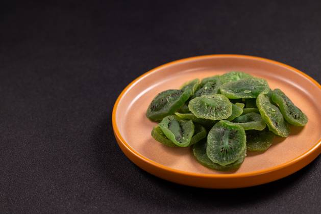 Getrocknete Kiwi-Scheiben auf einem braunen Teller Dried kiwi slices fanned on a rustic brown ceramic plate against a dark backdrop, vibrant green dehydrated fruit showcasing a healthy, sweet, vegan snack or baking ingredient (License=RF) Copyright: xZoonar.com VictoriaxKondysenkox(ArtSvitlynax 24165867