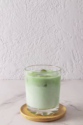 Ein großes Glas natürlichen Grüntee Matcha Latte steht auf einem Holzteller und einem weißen Marmortisch. Gesundheitsförderndes, belebendes Mittel A wide glass of natural green tea matcha latte stands on a wooden plate and a marble white table. health-improving, invigorating agent Copyright: imageBROKER MarinaxMoskalyuk ibxiqx14292192.jpg