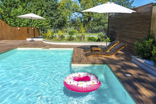 Hinterhofpool mit türkisfarbenem Wasser, Holzdeck, Sonnenschirmen, Liegestühlen und rosafarbenem Donut Float Backyard swimming pool with turquoise water, wooden deck, umbrellas, lounge chairs, and pink donut float Copyright: imageBROKER MariaxKraynova ibxiqx15511087.jpg