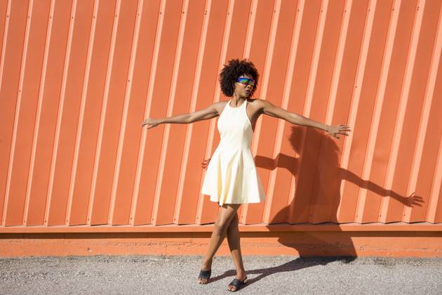 Happy woman with afro hairstyle in yellow dress dancing by orange wall model released, Symbolfoto, JSMF03464