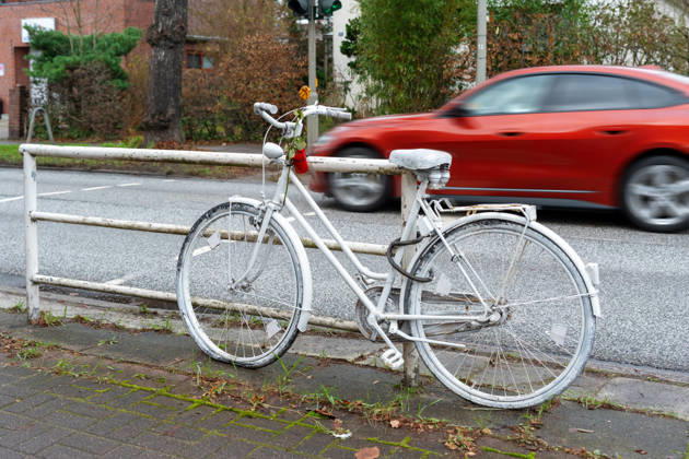 Hamburg, Germany - November 29, 2025: A white ghost bike on the side of the road commemorates a fatal traffic accident. Cars speeding by highlight the dangerous situation cyclists often face in heavy city traffic.