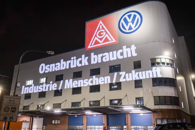 Projection of IG Metall logo and lettering Osnabrück needs industry people future next to the VW logo on the facade of the Osnabrück VW plant Peaceful protest rally of IG Metall in Osnabrück with on the situation automotive industry VW plant Osnabrück 08 12 2025 IG Metall rally in front of the VW plant Osnabrück